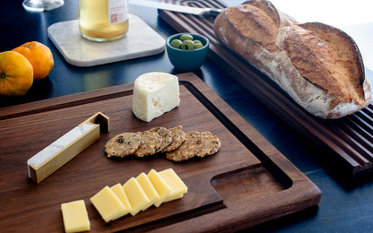 A wooden Fire Road Slope Carving Board with bread, cheese and olives.
