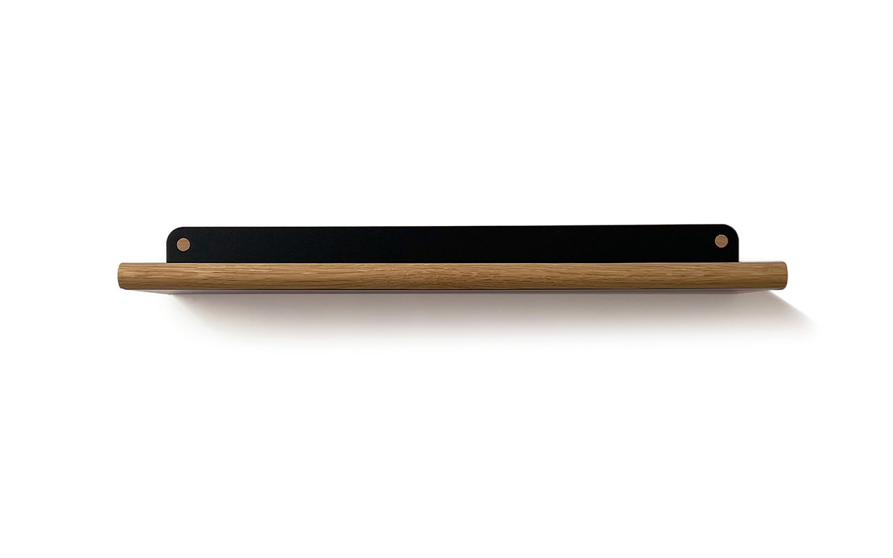 The Plane Wall Shelf, crafted from walnut wood, features a minimalist design supported by a sleek black metal bar. The steel support is precisely laser-cut for an elegant touch. This product is by Fire Road.