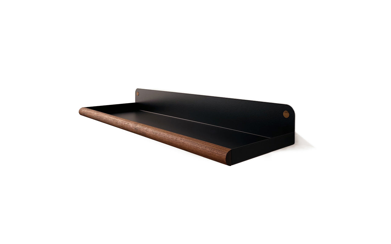 A minimalist Fire Road Plane Wall Shelf featuring a black metal base made of laser-cut steel and a wooden front rail crafted from walnut wood, set against a white background.