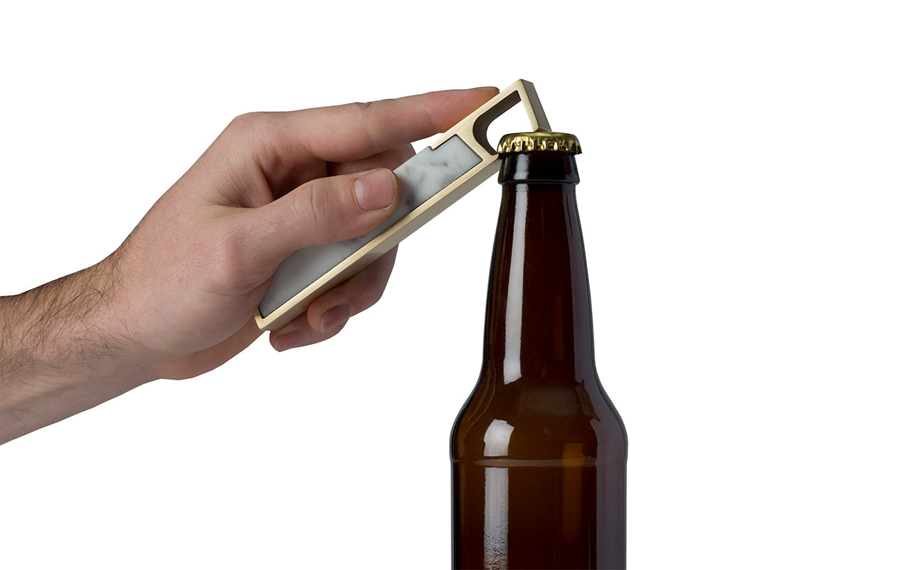A person opening a beer bottle with a Fire Road Profile Bottle Opener.