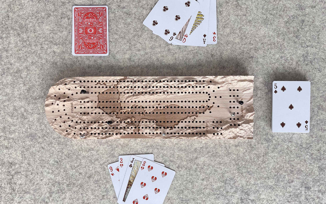 A set of playing cards and a Fire Road Terrain Cribbage Board on a table.