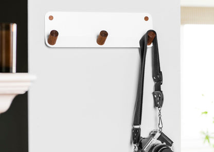 white powder coated steel wal hook with 3 walnut pegs in space with camera strap